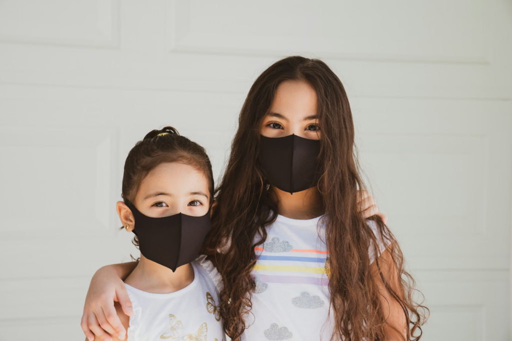 Two girls wearing black face masks with arms on each other's shoulders.